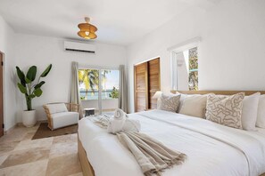 A hotel room with a large bed, a sitting area with a chair, a potted plant, and a view of the outdoors. - Cataño Ocean View | Coastal Living Near OSJ Ferry (Cataño)
