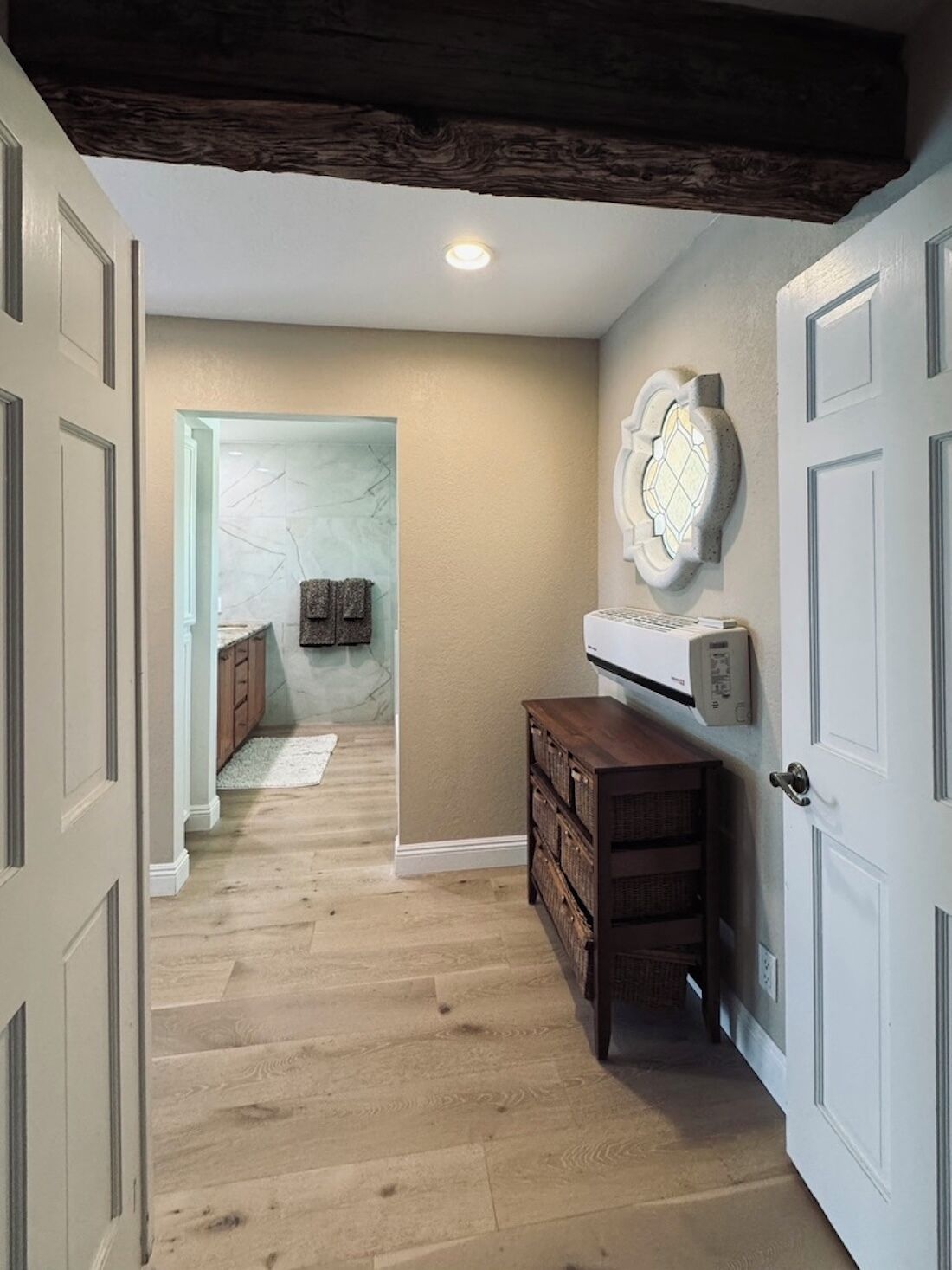 A hallway with wooden flooring, a built-in bench, a wall-mounted light fixture, and a door with a decorative glass panel.