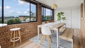A modern dining area with a wooden table, white chairs, and a large window offering a view of the neighborhood.