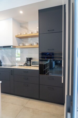 A modern kitchen with dark cabinetry, a glass backsplash, and a built-in oven. - Luxurious Sunset Lagoon View 2-bed bedroom Apartment (Cole Bay)