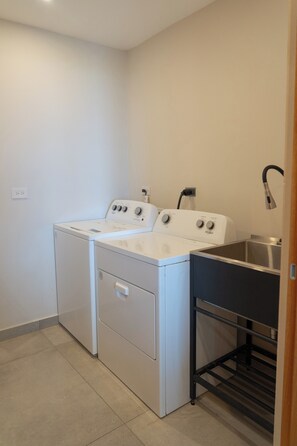 A laundry room with a front-loading washer and dryer, a sink, and a metal rack. - Luxurious Sunset Lagoon View 2-bed bedroom Apartment (Cole Bay)