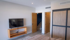 A modern living room with a flat-screen TV on a wooden stand, a patterned rug, and a sofa with multiple cushions. - Luxurious Sunset Lagoon View 2-bed bedroom Apartment (Cole Bay)