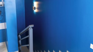 A staircase with a metal handrail and a blue wall with two wall-mounted light fixtures. - Luxurious Sunset Lagoon View 2-bed bedroom Apartment (Cole Bay)