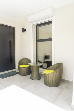 A modern outdoor seating area with wicker chairs and a glass table, adjacent to a sliding glass door leading to a balcony. - Luxurious Sunset Lagoon View 2-bed bedroom Apartment (Cole Bay)