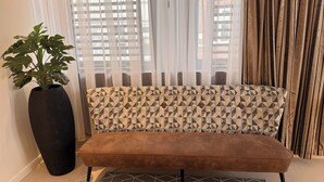 Ein Zimmer mit einem gemusterten Sofa, einem großen Topfpflanzen und durchsichtigen Vorhängen.