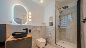 Ein modernes Badezimmer mit großem Spiegel, einem schwarzen Hängebecken, einer Toilette und einer Duschkabine.