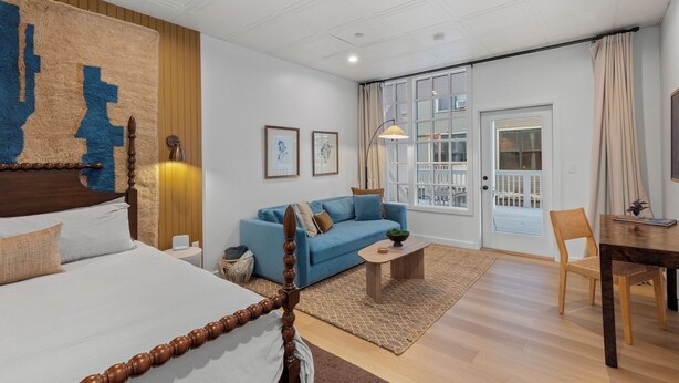Une chambre d’hôtel moderne avec un grand lit, un canapé bleu, une table basse en bois et une table à manger avec des chaises.