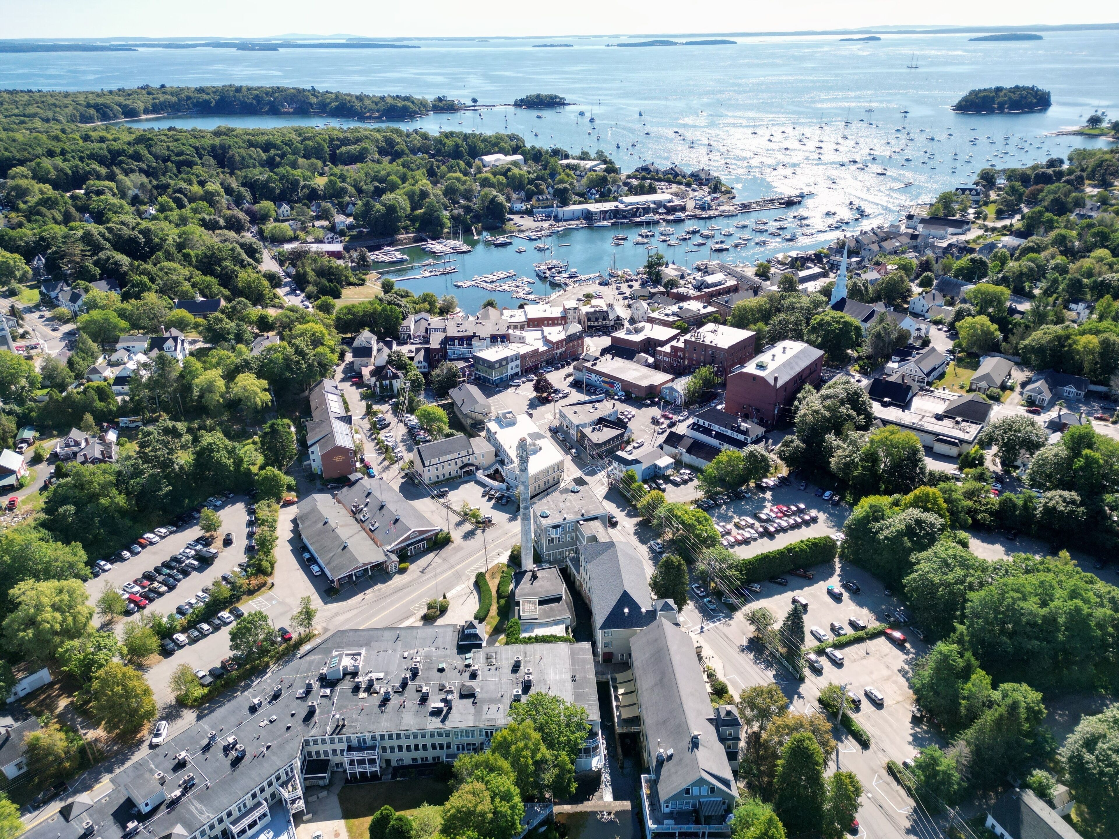 An aerial view of a coastal town with a marina, buildings, and surrounding greenery.