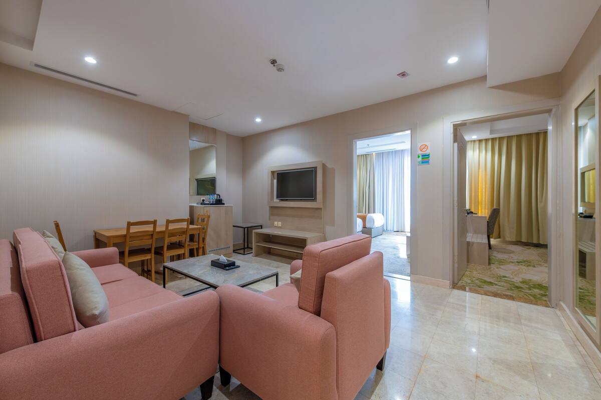 A modern living room with a pink sofa, a TV, a dining area with wooden furniture, and a glass door leading to a balcony.