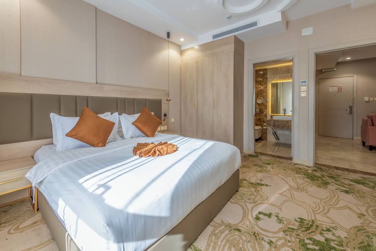 A modern hotel room with a large bed, a wooden headboard, and a patterned carpet.