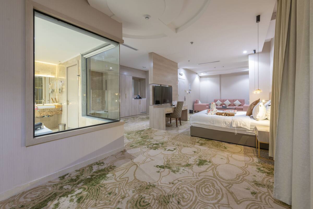 A modern hotel room with a large mirror, a bed with a pink headboard, a desk, and a television.