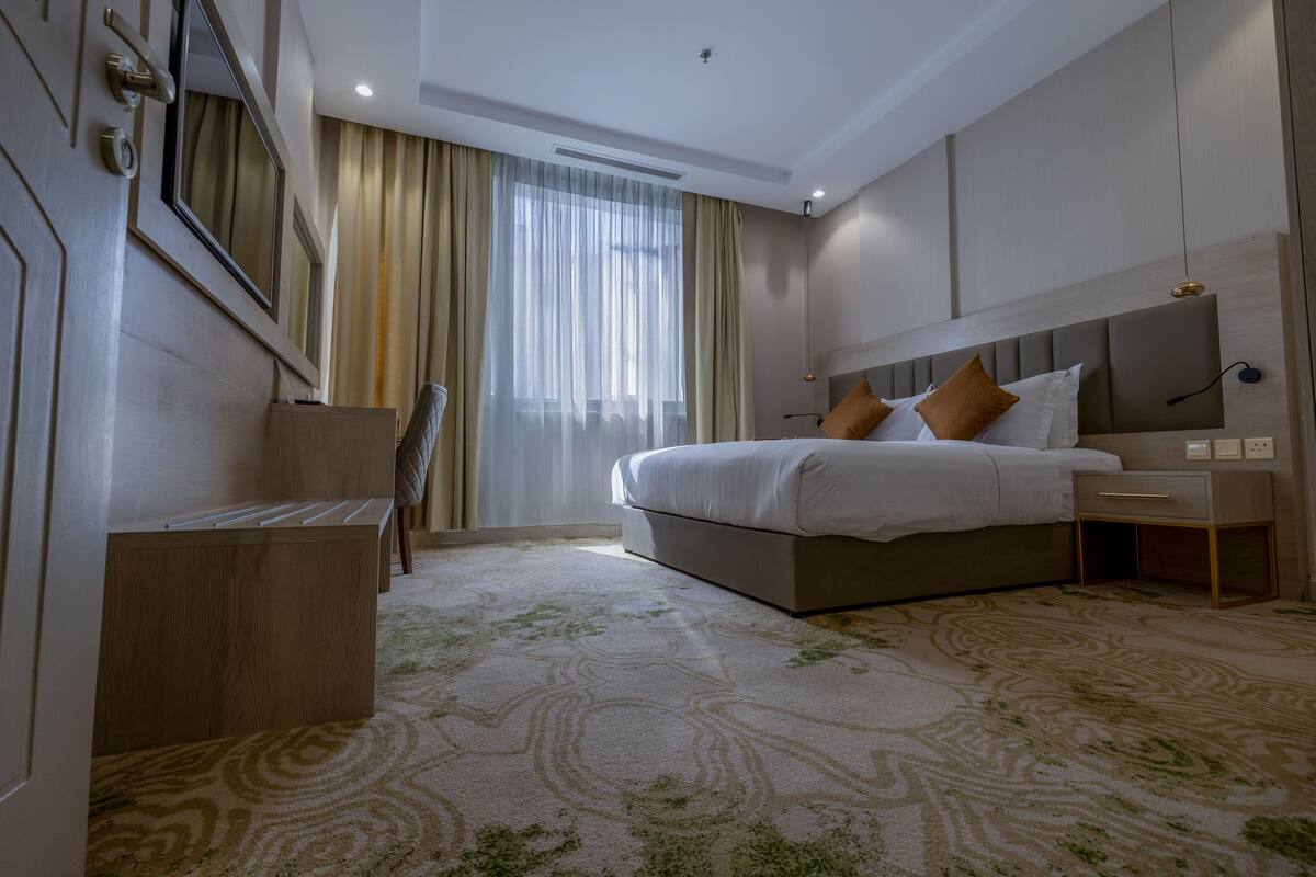 A modern hotel room with a large bed, a desk, and a window with curtains.