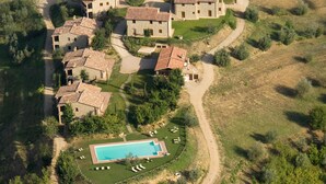 Vista aérea de uma área residencial com vários edifícios de pedra, uma piscina e vegetação ao redor.