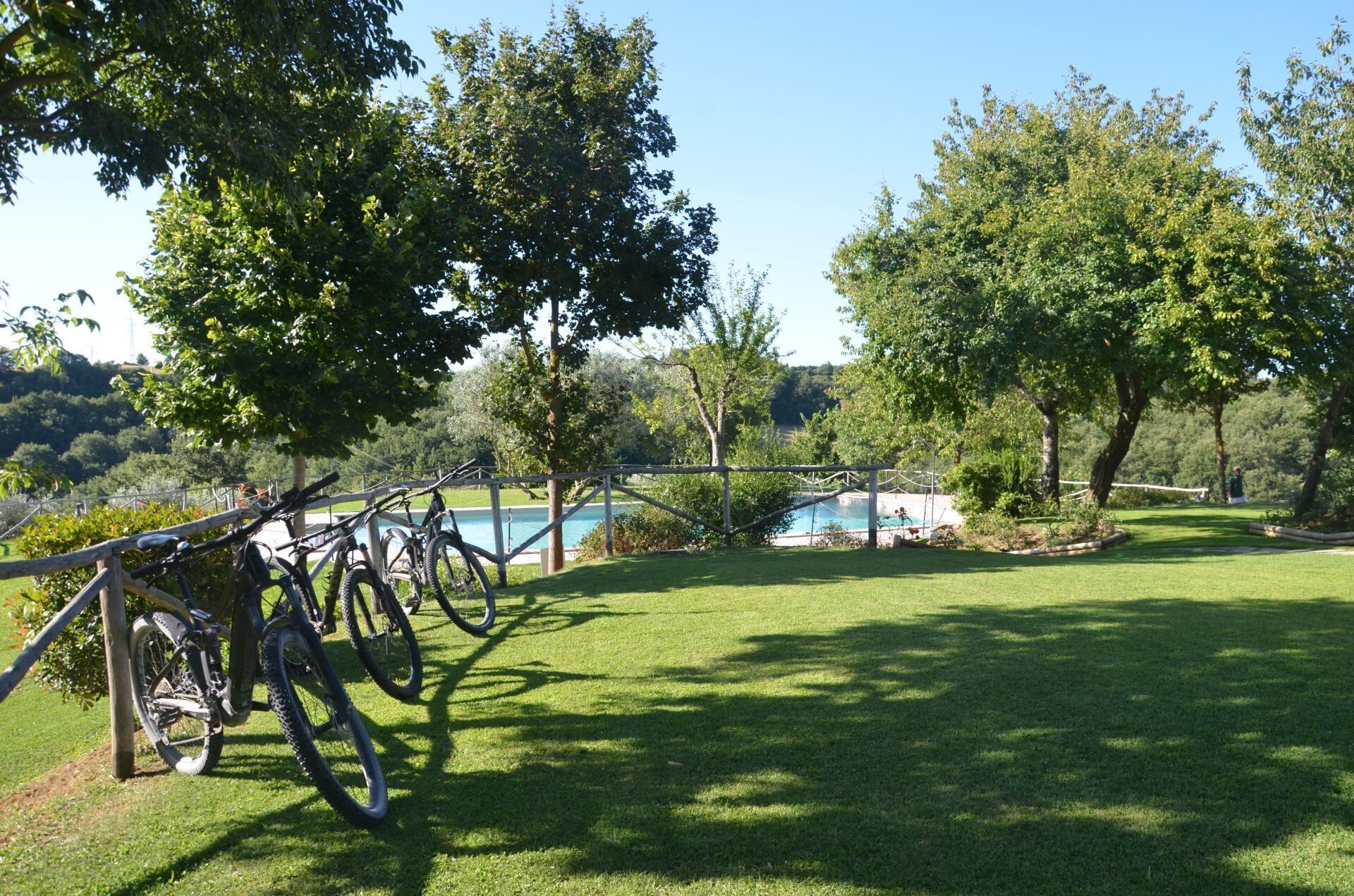 Zona verde con bicicletas estacionadas cerca de una valla, con vista a una piscina y árboles.