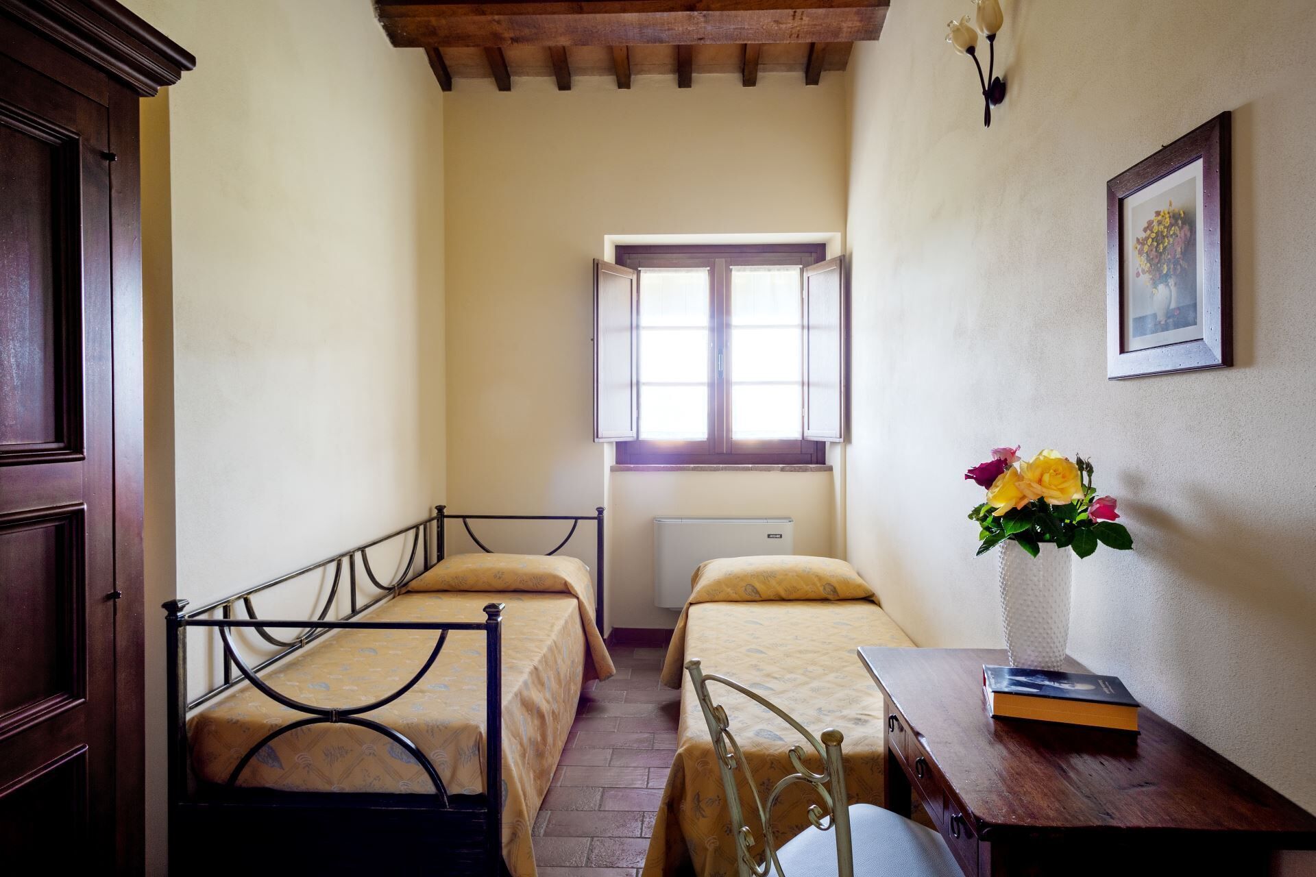Une petite chambre agréable, dotée de deux lits simples, d’un bureau avec une chaise, d’un radiateur et d’une fenêtre donnant sur un beau paysage.