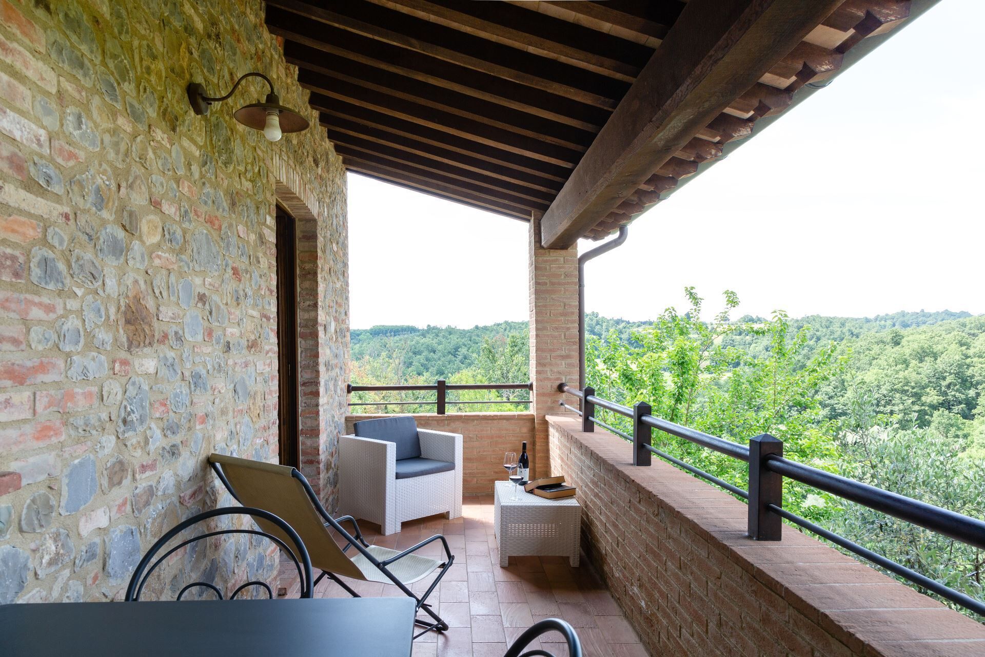 Un balcon avec des murs en pierre, un canapé en osier, une chaise et une petite table sur laquelle se trouvent une bouteille et des verres.