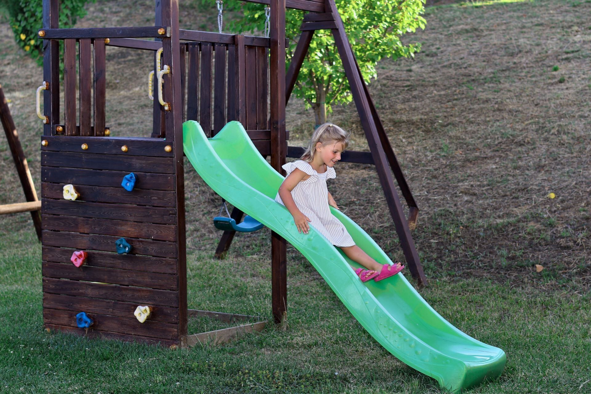 Une structure de jeu en bois avec un toboggan vert et des prises d’escalade.