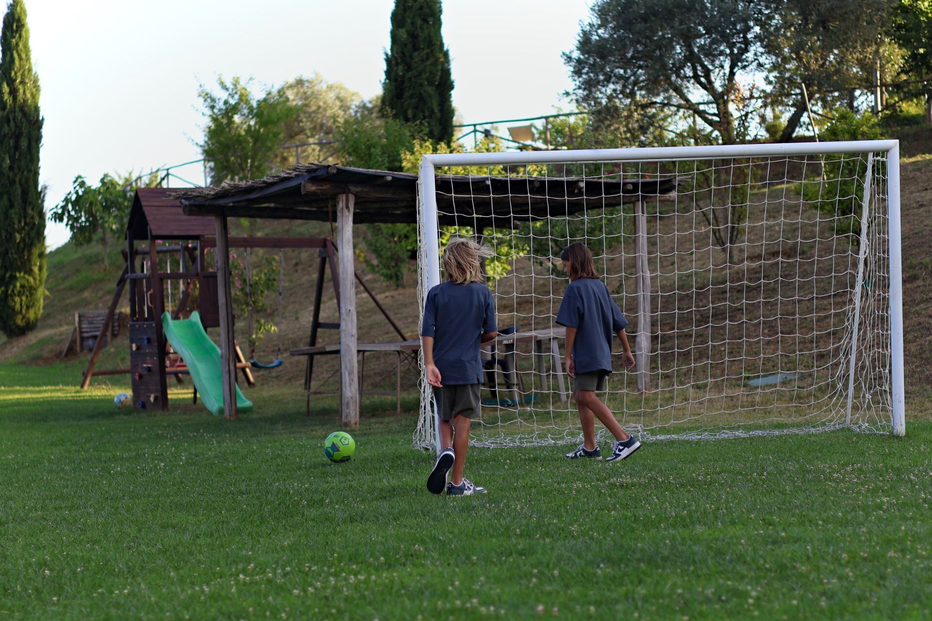 A soccer goal in a grassy field with a wooden play structure in the background.