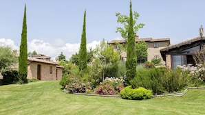A stone house with a tiled roof, surrounded by a well-maintained lawn and various flowering plants. - Two-bedroom apartment with private entrance (Città della Pieve)