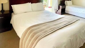Una habitación de hotel con una cama grande, dos mesitas de noche, un ventilador de techo y una ventana con cortinas.
