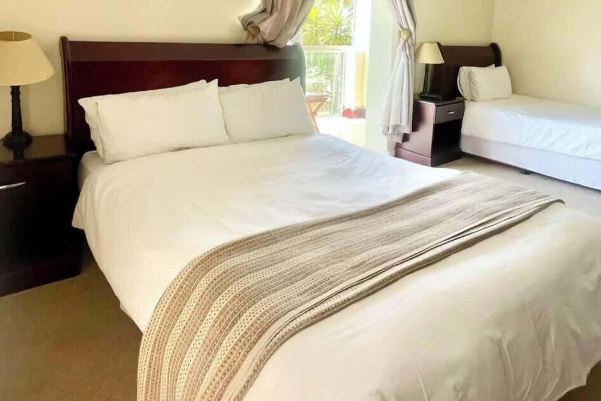Une chambre d’hôtel avec un grand lit, deux tables de chevet, un ventilateur de plafond et une fenêtre avec des rideaux.
