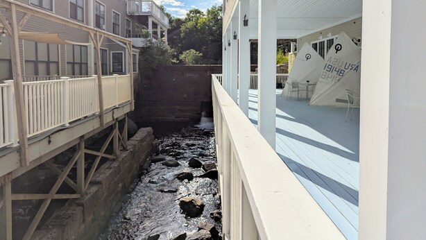 Un étroit canal bordé de bâtiments, avec une passerelle en bois d’un côté et un bâtiment blanc doté d’une terrasse extérieure de l’autre.