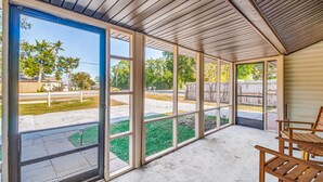 Une terrasse couverte avec de grandes fenêtres, un sol en béton et des chaises en bois.