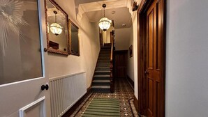 Un couloir avec un tapis à motifs, un escalier et une porte en bois.