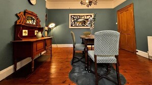 Une salle à manger avec une table en bois, des chaises, un lustre, une horloge et un tableau accroché au mur.