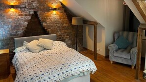 Une chambre avec un mur en briques, un lit recouvert d’une couvre-lit à motifs, une chaise et une lampe.