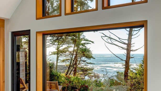 Un interior moderno con amplios ventanales que ofrecen vistas al océano, una terraza de madera y un rincón de estar acogedor.