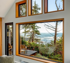 A modern interior with large windows offering ocean views, a wooden deck, and a cozy seating area. - Fogged Inn Cabin (Ucluelet)