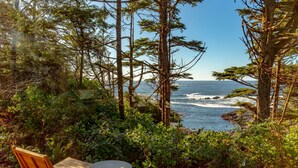 A wooden deck with a table and chairs overlooking the ocean, surrounded by dense foliage and tall trees. - Fogged Inn Cove (Ucluelet)
