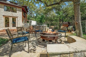 A stone patio with outdoor furniture, a fire pit, and a stone building in the background.