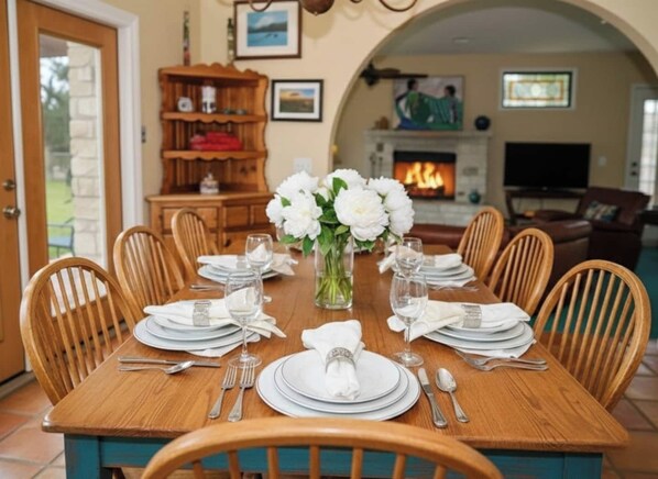 A dining table set for eight with white plates, silverware, and a vase of white flowers.