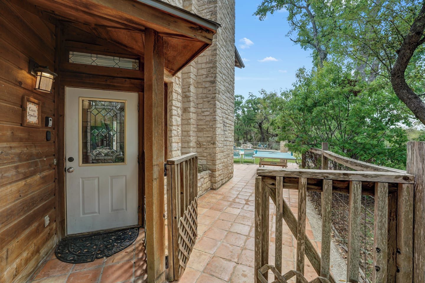 A wooden exterior with a stone wall, a door with a stained glass window, and a wooden deck with a pool table.