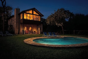A two-story stone house with a swimming pool and lounge chairs.