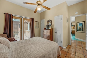 A bedroom with a bed, a ceiling fan, a dresser, and a door leading to a balcony.