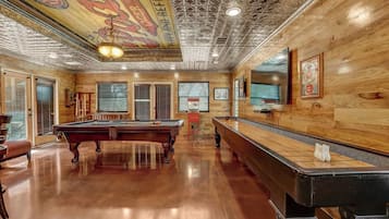 A pool table in a room with wooden walls and a ceiling with a geometric pattern.