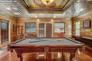 A pool table with cues and balls, wooden walls, and a ceiling with a decorative design.
