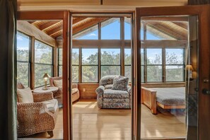 Une pièce chaleureuse avec un plafond en bois, de grandes fenêtres, un canapé, un fauteuil et un lit.