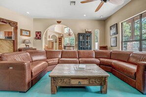 A spacious living room with a large brown leather sectional sofa, a wooden coffee table, and a ceiling fan.