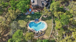 Una propietat residencial amb piscina, un porxo cobert i una casa espaiosa envoltada d'arbres.