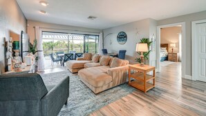A spacious living room with a large sectional sofa, a coffee table, and a dining area with chairs. There is a large window providing natural light and a view of the outdoors. - Walk to the Beach! Canal-Front Marco Island Home (Marco Island)