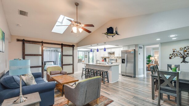 A spacious living area with a sofa, coffee table, and a dining table with chairs. A kitchen with a refrigerator and bar stools is visible in the background. - Walk to the Beach! Canal-Front Marco Island Home (Marco Island)