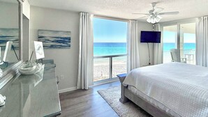 A bedroom with a large bed, a ceiling fan, a TV, and a view of the beach. - Steps to Beach: Oceanfront w/ Panoramic Gulf Views (Destin)