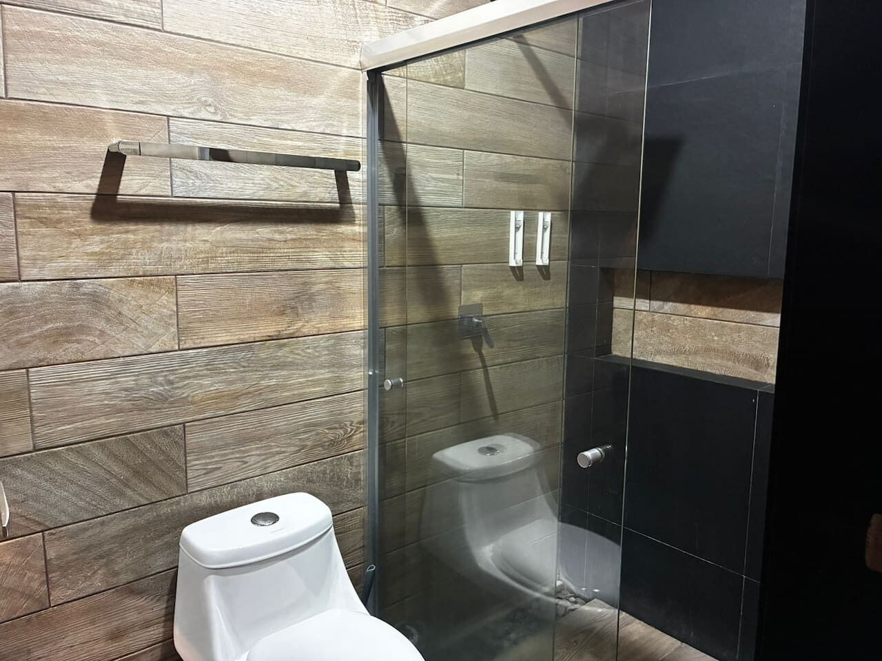 Ein modernes Badezimmer mit einer Wandgestaltung aus Holz, einer Duschkabine aus Glas und einer weißen Toilette.