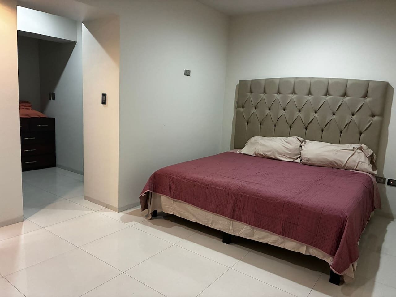 Une chambre à coucher avec un lit, une tête de lit et une porte donnant sur une autre pièce.