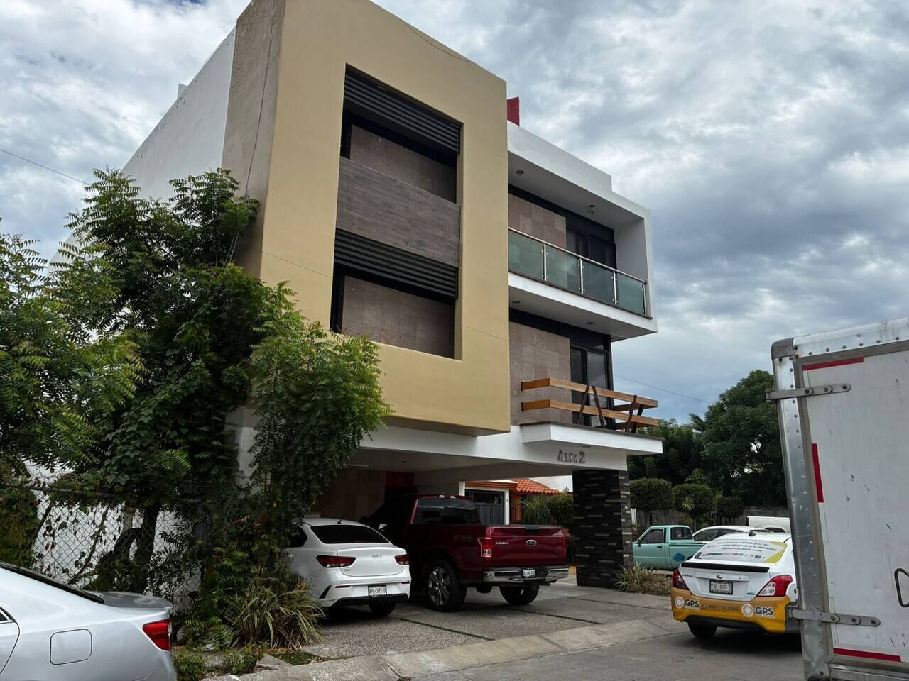 Un edificio moderno con techo plano, un balcón en el segundo piso y entrada a un garaje.