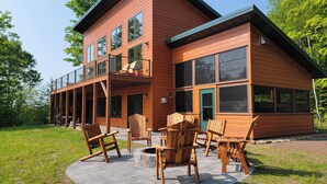 Eine zweistöckige Holzhütte mit Balkon, Sitzgelegenheit im Freien und einem Feuerkorb.